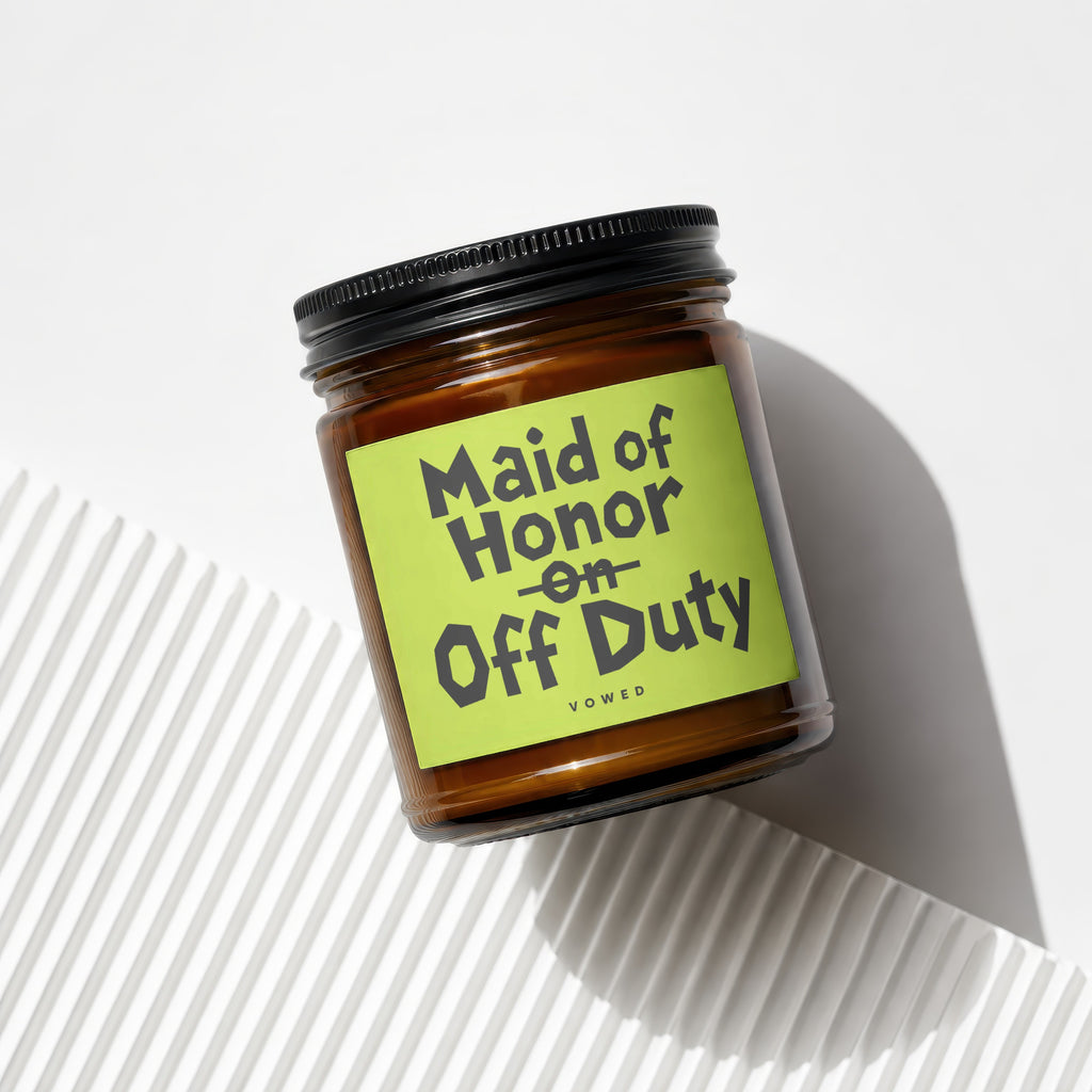 Amber glass candle with 'Maid of Honor on Off Duty' text on a bright green label.