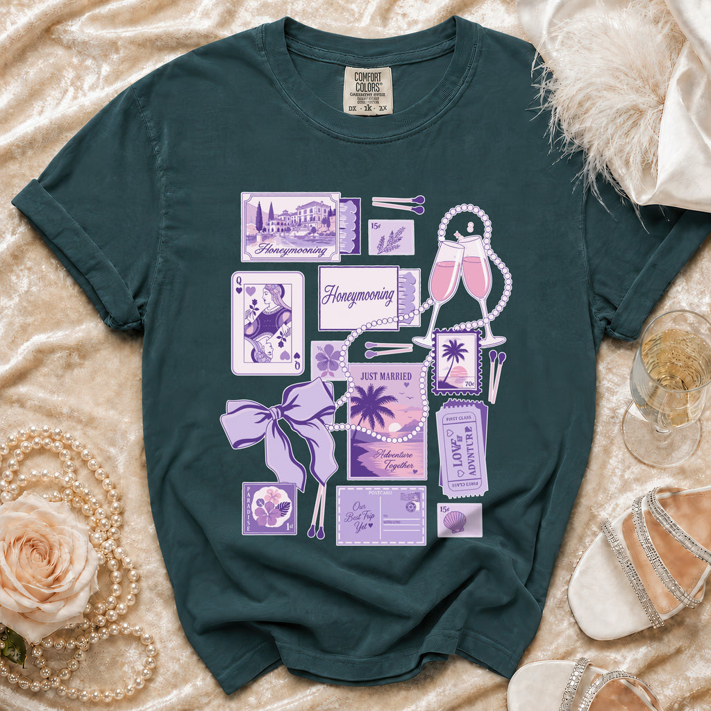 Dark teal t-shirt with "Honeymooning" graphics including postcards, playing cards, champagne, and pearls.