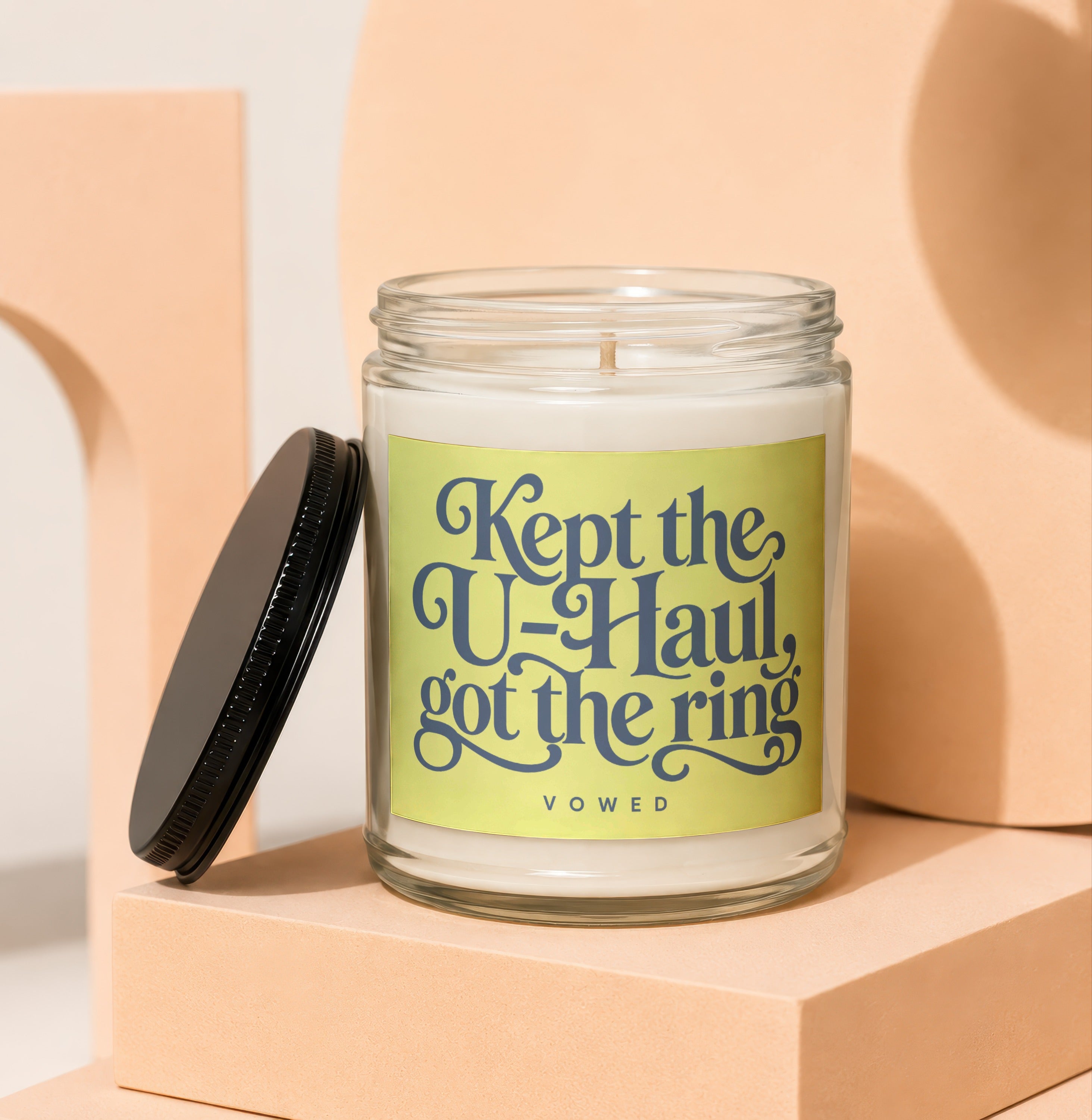 Glass candle with yellow label reading "Kept the U-Haul, got the ring"