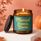 Amber jar candle with lit wick and turquoise label reading "Married. Iconic. Done. VOWED."