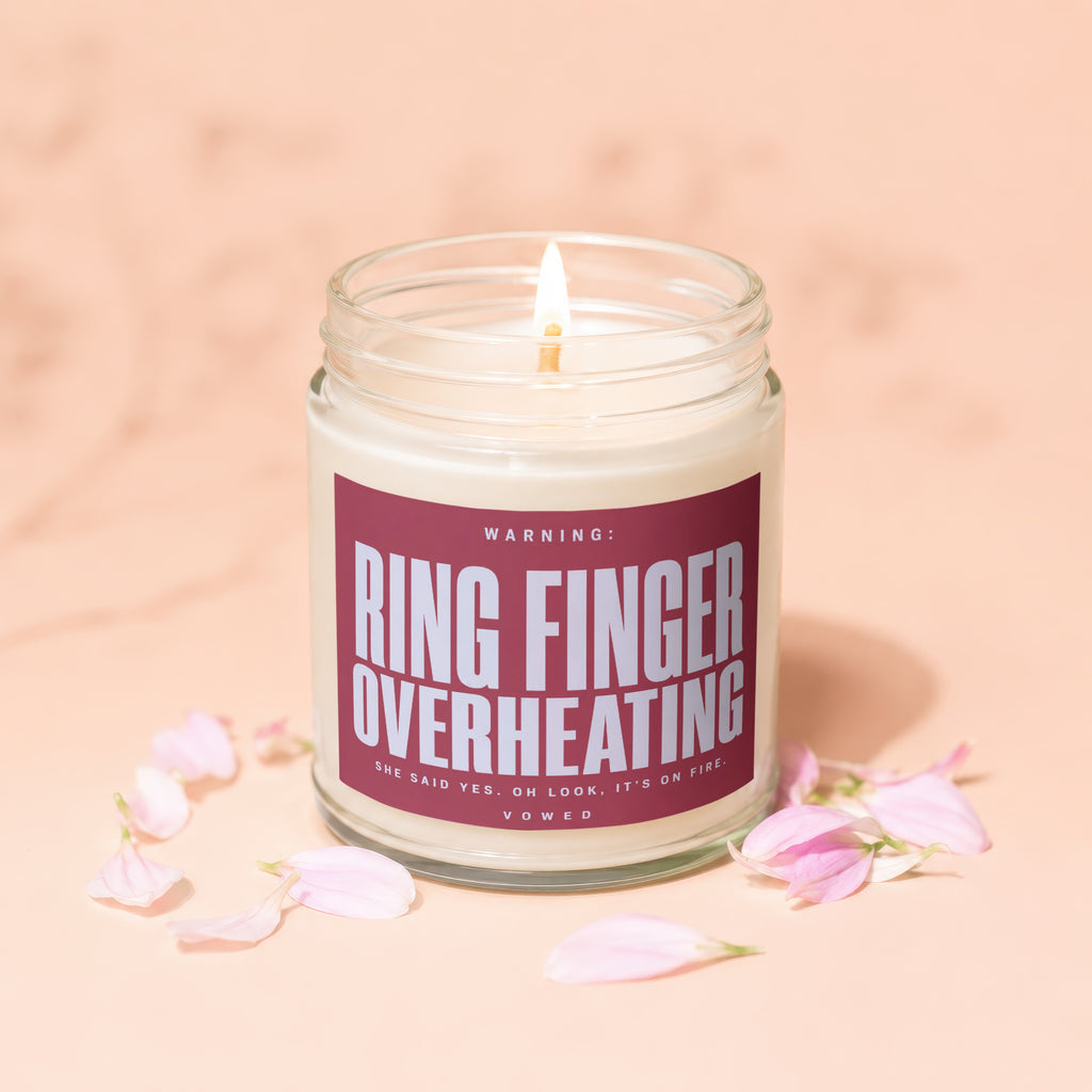 Candle with "Ring Finger Overheating" warning label, surrounded by pink petals.