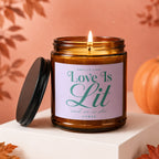 Amber jar candle with a lit flame, reads "Smells Like Love Is Lit and so is she VOWED".