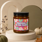 Amber jar candle with "Proposal of the Year!" text on floral label.