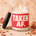 Lit candle in glass jar with red label reading "TAKEN AF. VOWED".