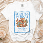 White t-shirt with "Reckless in Texas" stamp, cowboy boots, cactus, and hat.