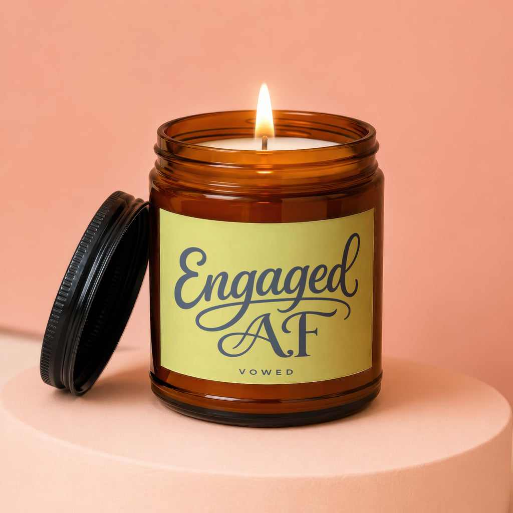 Amber jar candle with lit wick and lid off, displaying "Engaged AF VOWED".