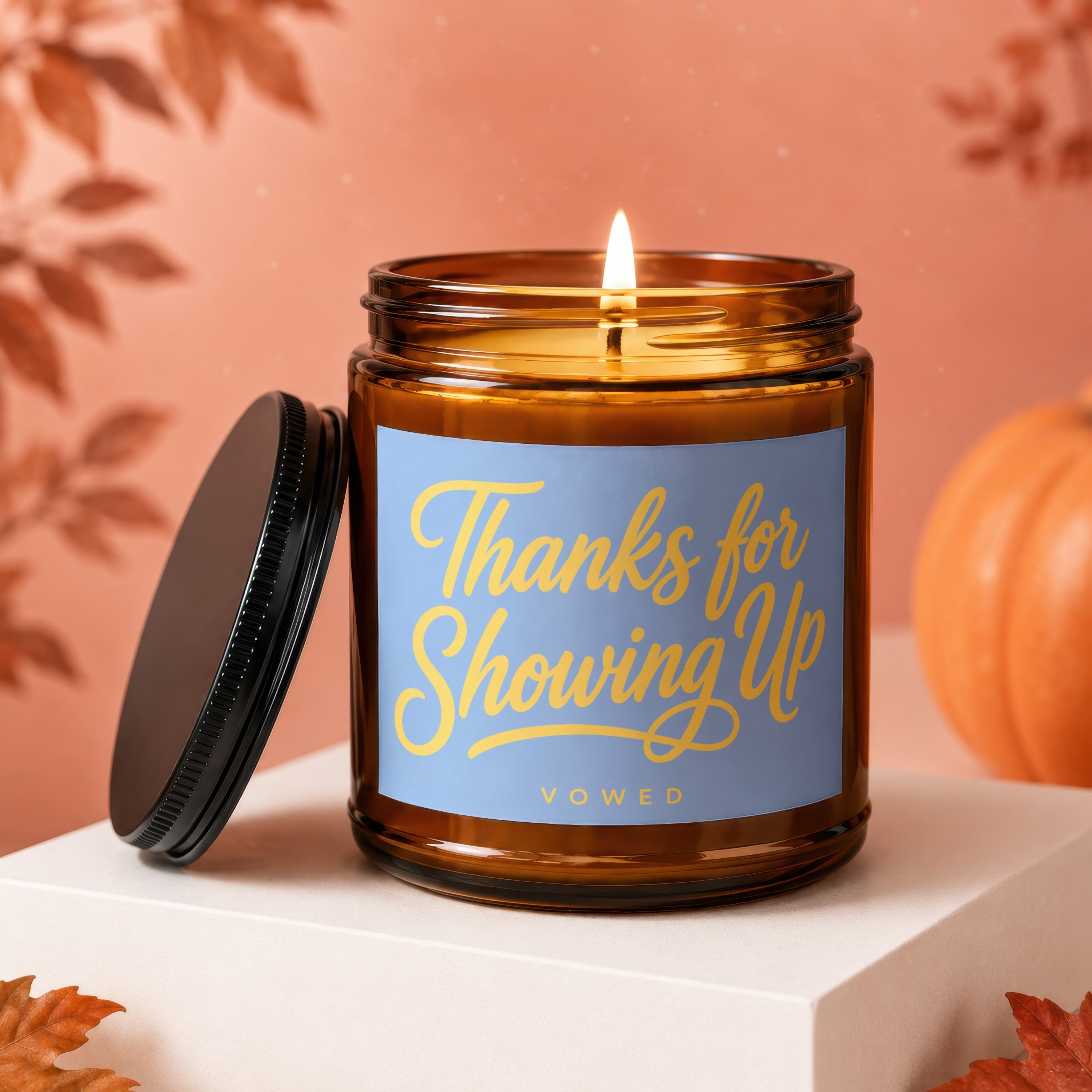 Amber candle with lit flame, blue label saying "Thanks for Showing Up" by Vowed.