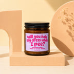 Amber jar candle with lilac label reading "will you hold my dress while I pee?"