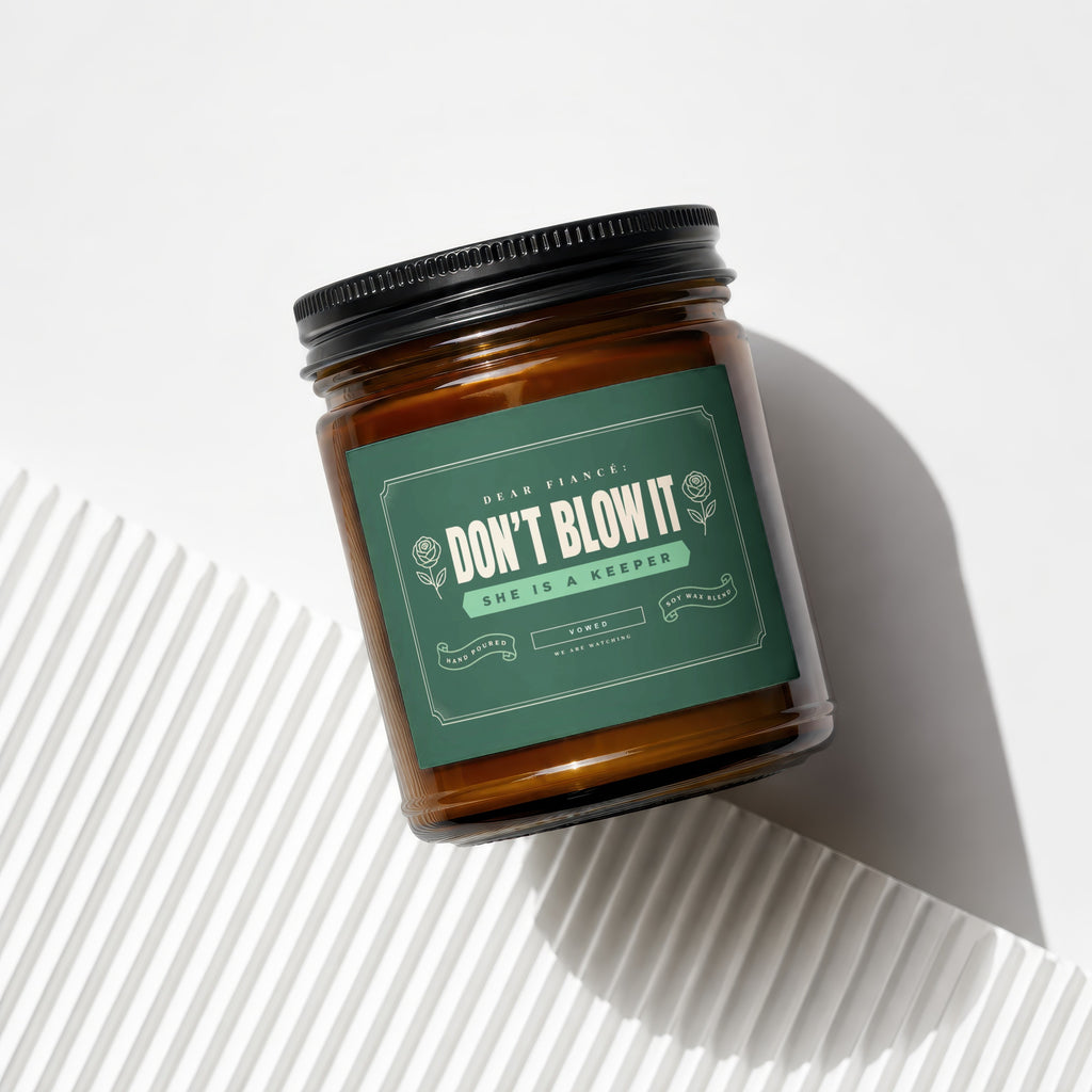 Amber jar candle with dark lid, green label reads "Dear Fiancé: Don't Blow It She is a Keeper".