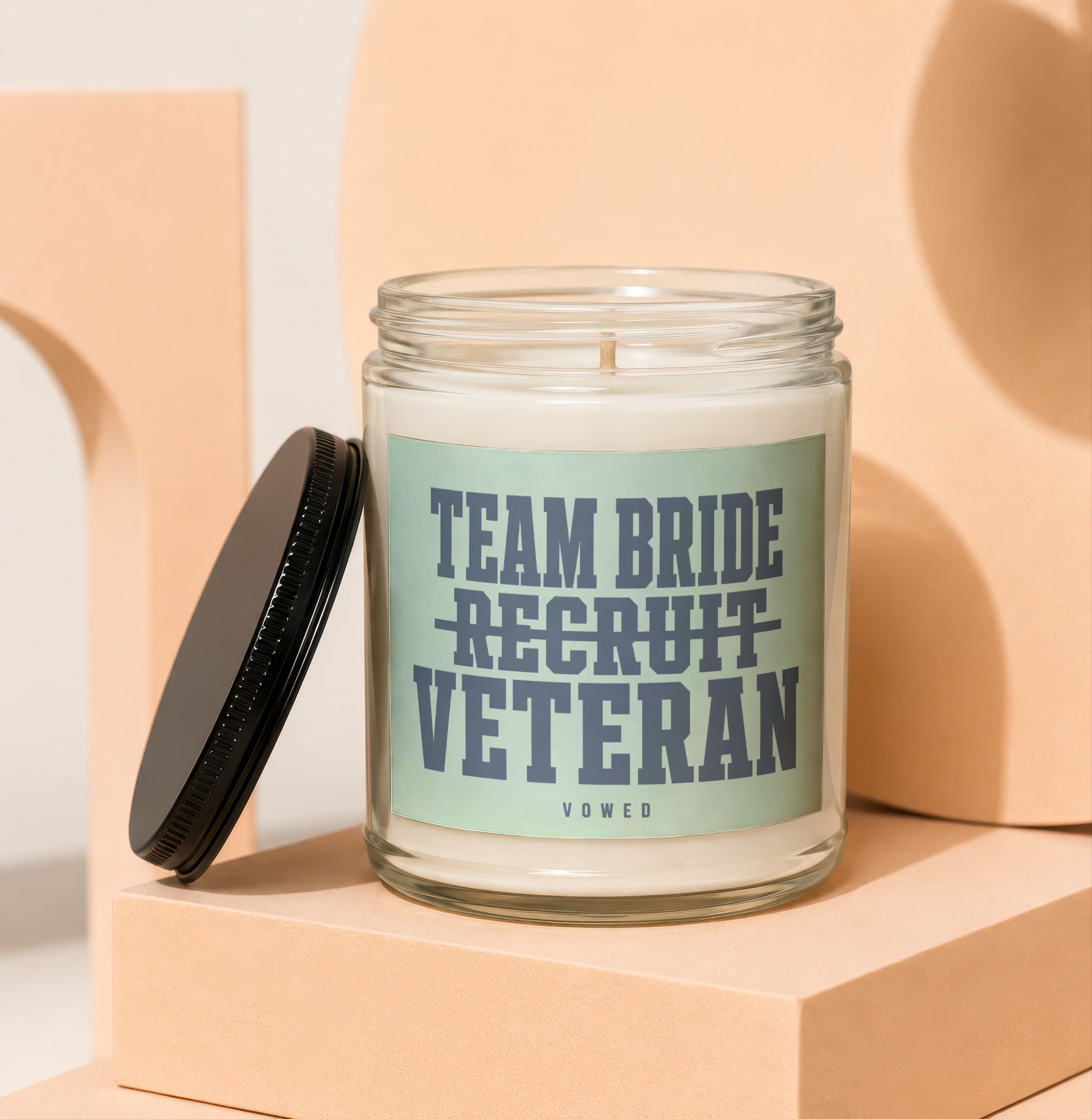 Glass candle with a label reading "Team Bride Recruit Veteran" and "Vowed".