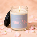 Lit candle in glass jar with "Future Mrs." text on label, surrounded by pink petals.