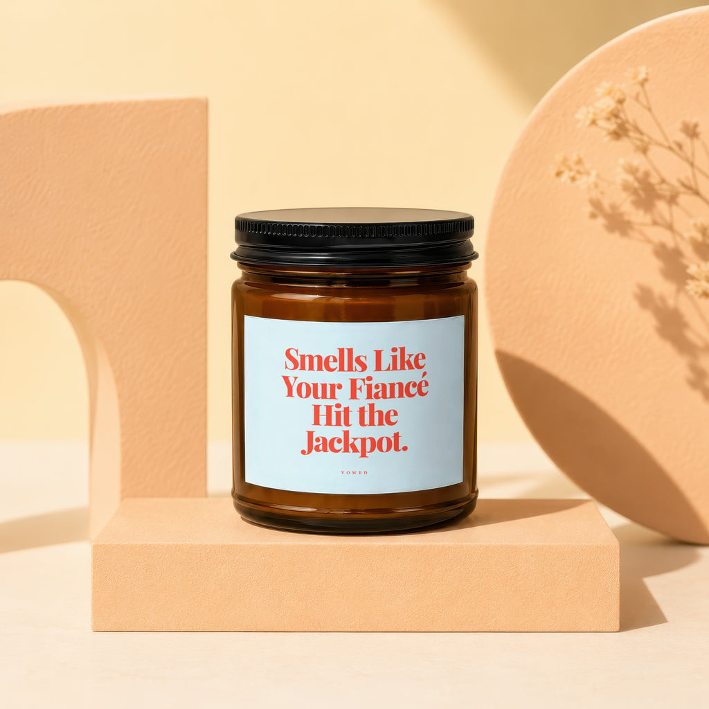 Amber jar candle with black lid, "Smells Like Your Fiancé Hit the Jackpot" text.