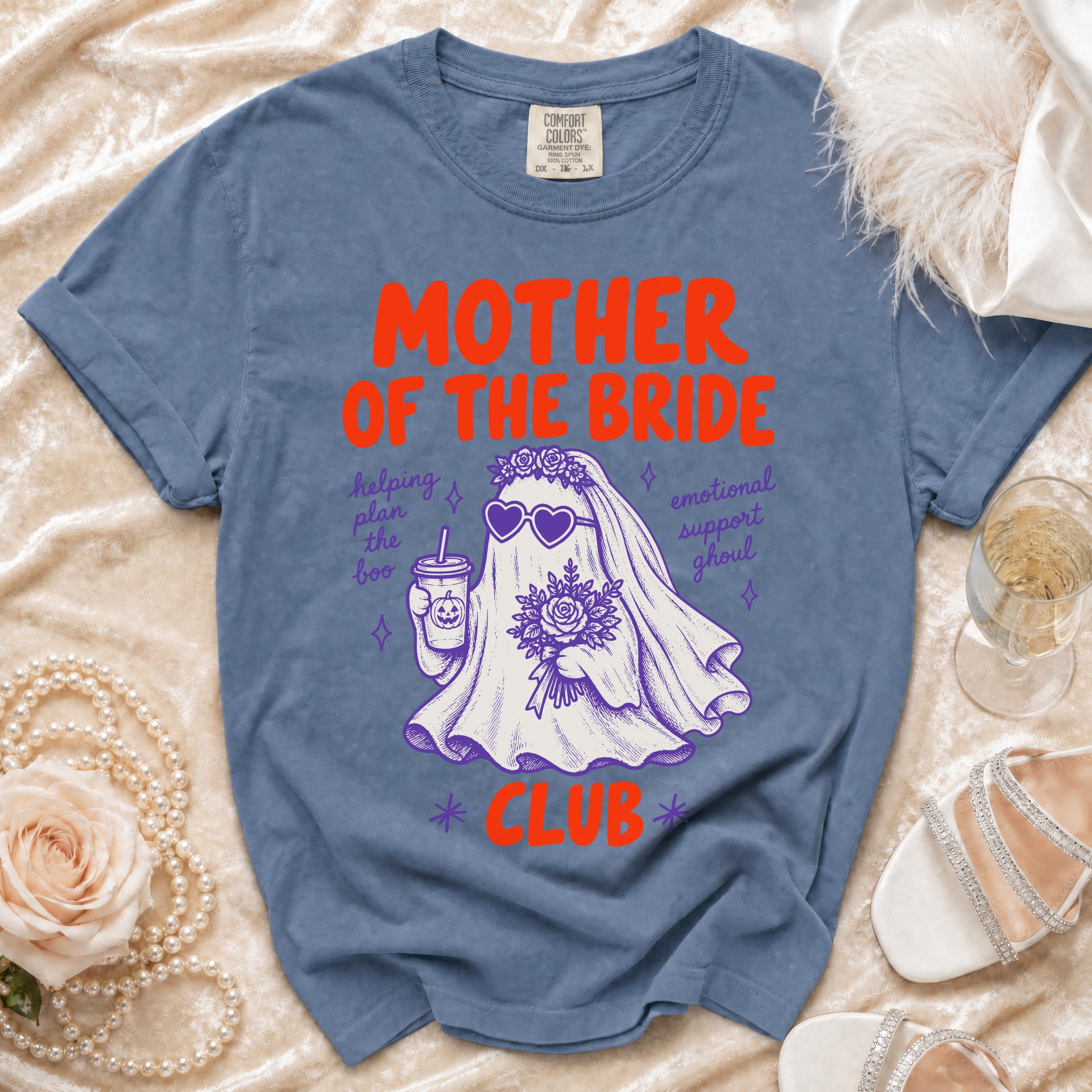 Blue t-shirt with "Mother of the Bride Club" ghost graphic, holding drink and flowers.