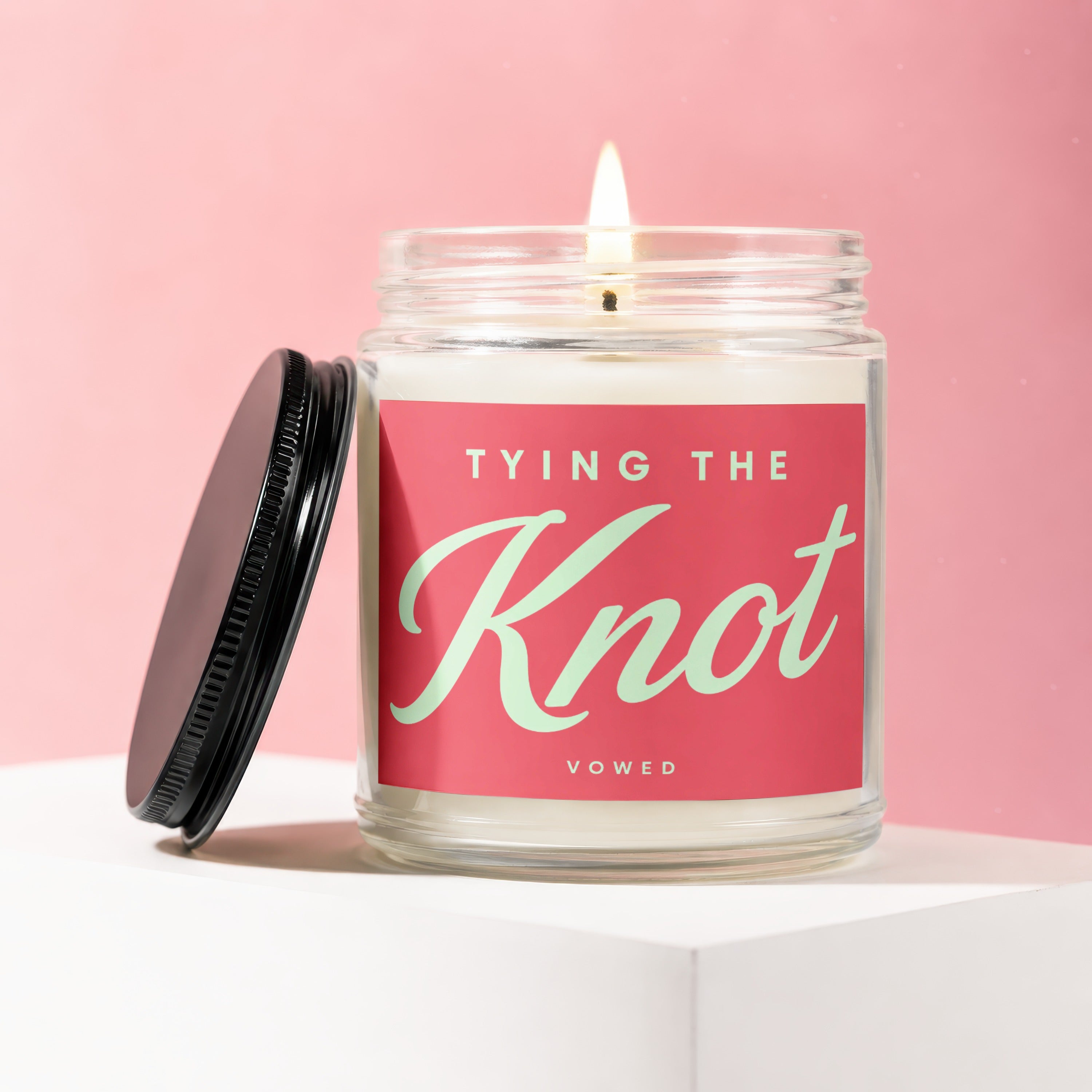 Burning candle in glass jar with "Tying The Knot" and "Vowed" text.