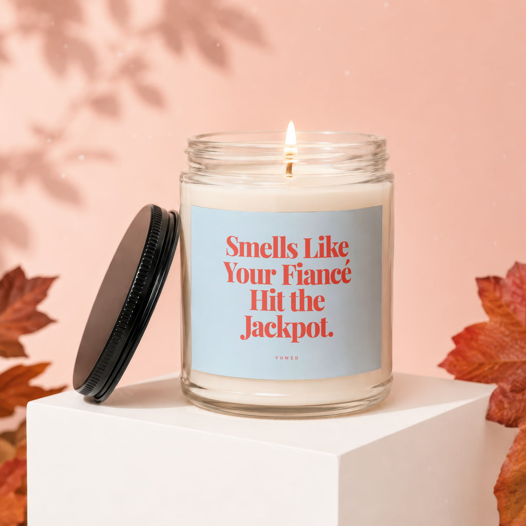 Candle with "Smells Like Your Fiancé Hit the Jackpot" text, lit wick, lid off.