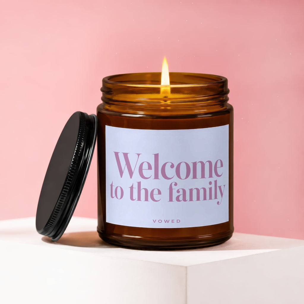 Amber candle with a lit wick reads "Welcome to the family" and "vowed."