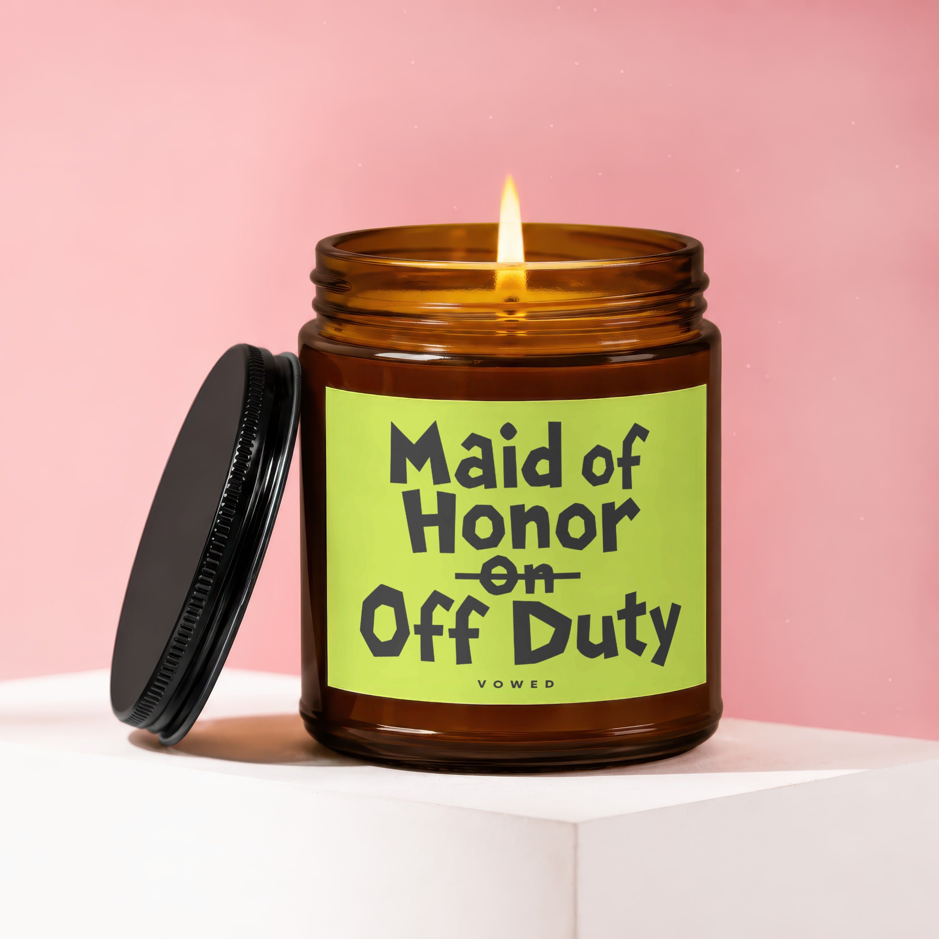 Amber glass candle with a lit wick and a black lid, labeled "Maid of Honor on Off Duty".