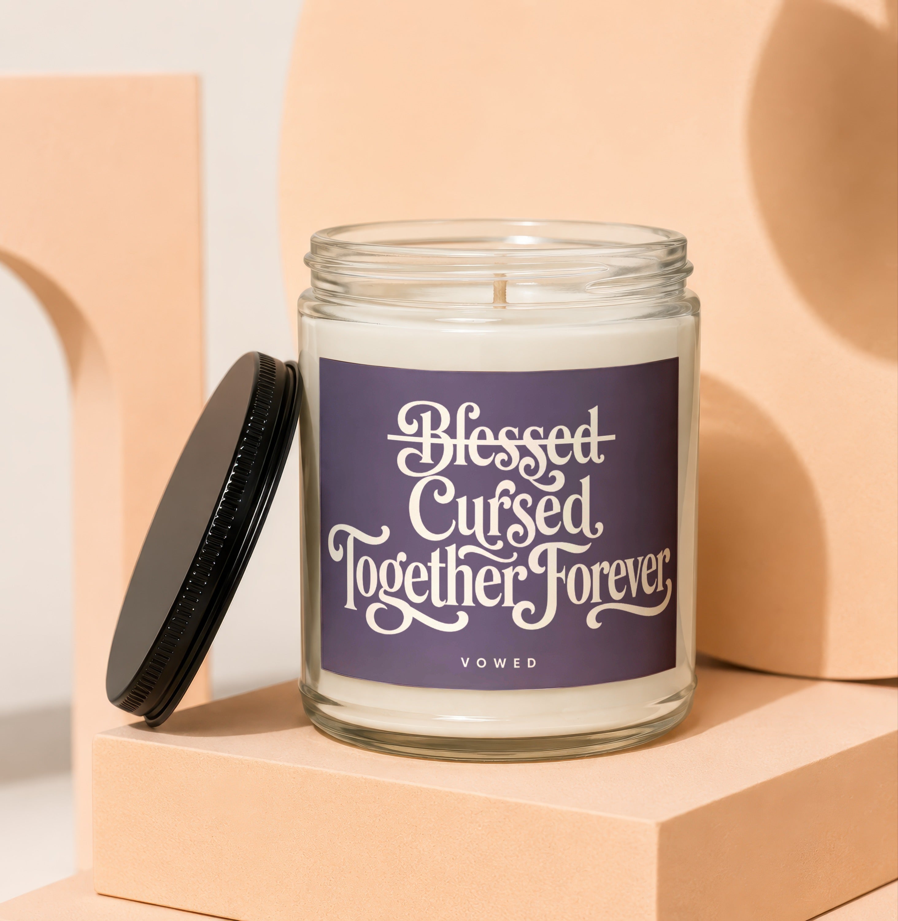 Glass candle with purple label reading "Blessed Cursed Together Forever VOWED".