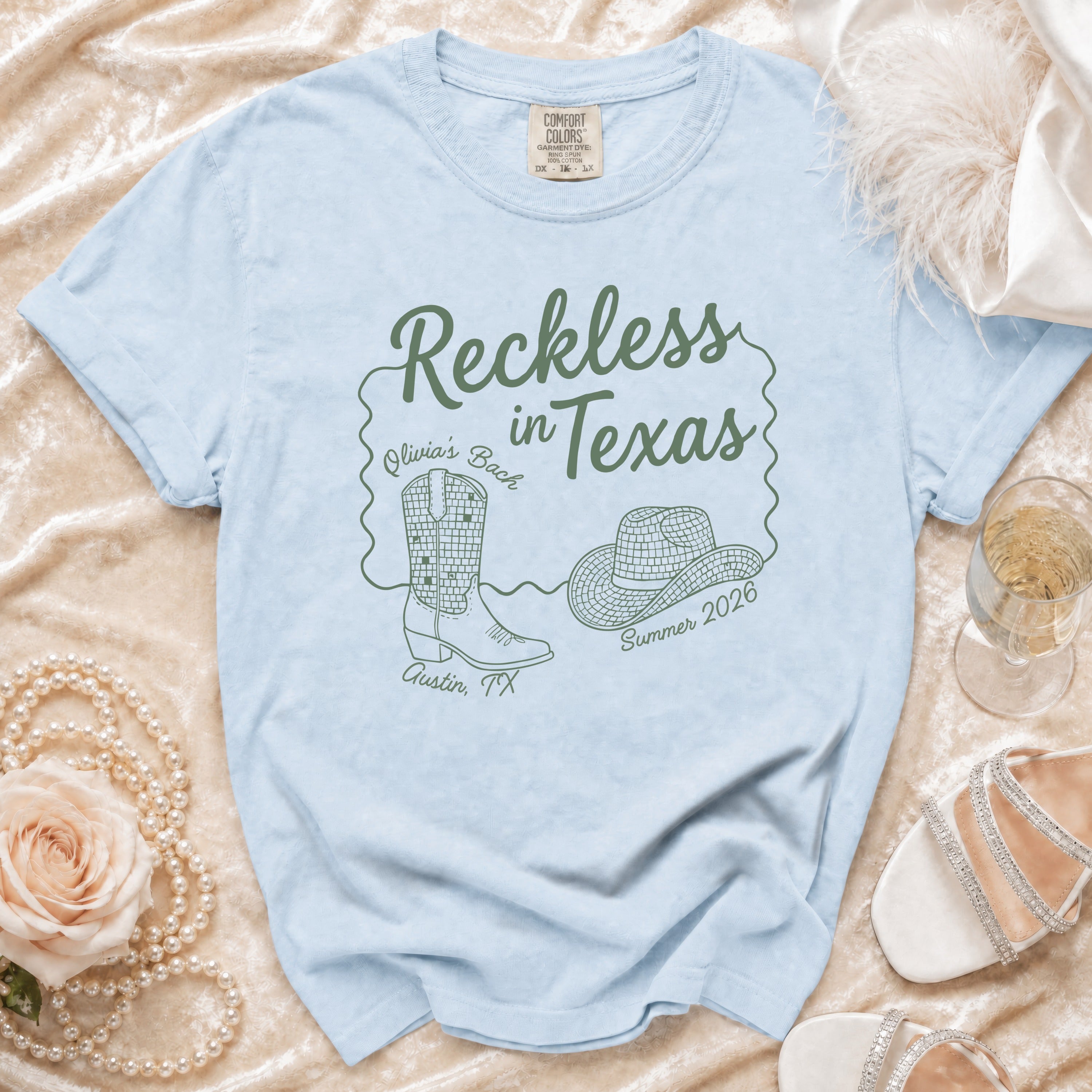 Light blue t-shirt with "Reckless in Texas" design, cowboy boots, and hat.