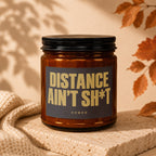 Amber glass candle with black lid and label reading "DISTANCE AIN'T SH*T VOWED".