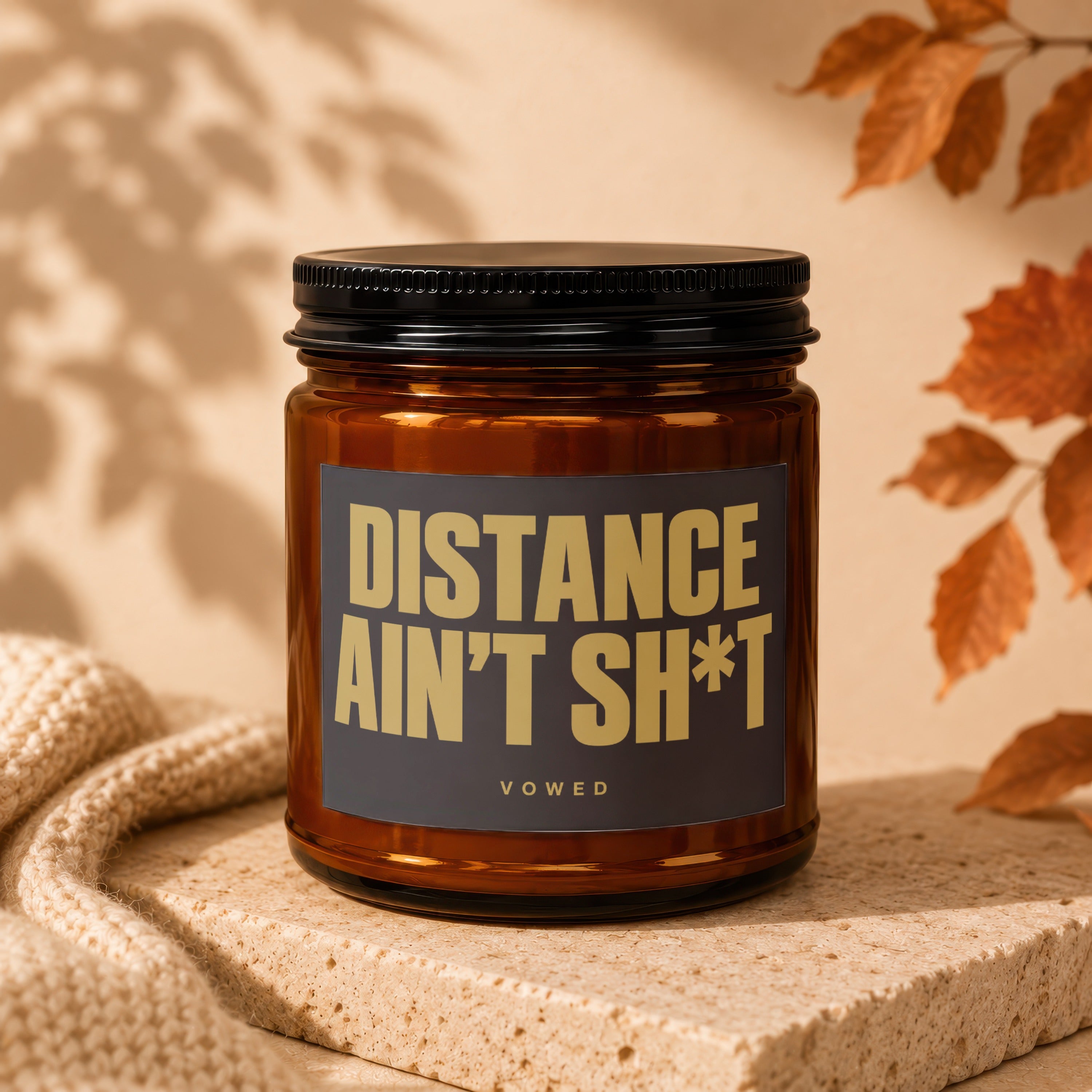 Amber glass candle with black lid and label reading "DISTANCE AIN'T SH*T VOWED".