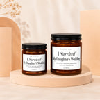 Two amber glass candles with black lids, labeled "I Survived My Daughter's Wedding."