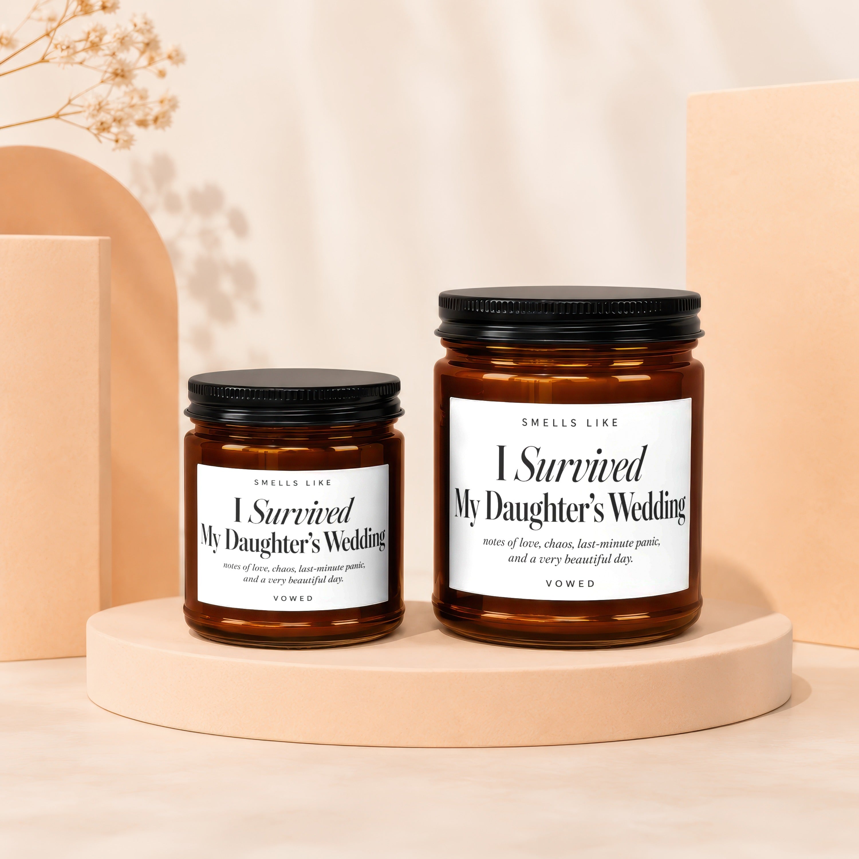 Two amber glass candles with black lids, labeled "I Survived My Daughter's Wedding."