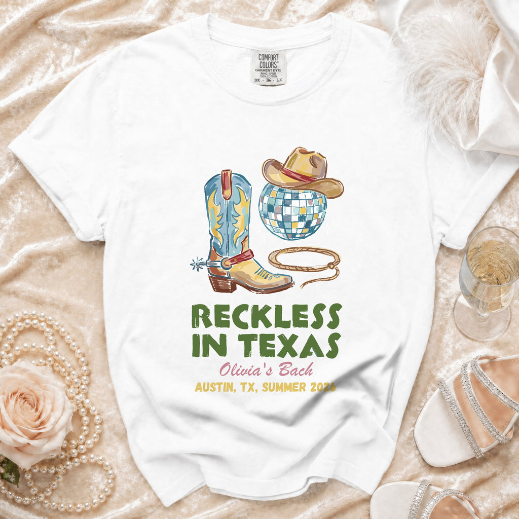 White t-shirt with cowboy boot, hat, disco ball, and text "Reckless in Texas".