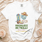 White t-shirt with cowboy boot, hat, disco ball, and text "Reckless in Texas".