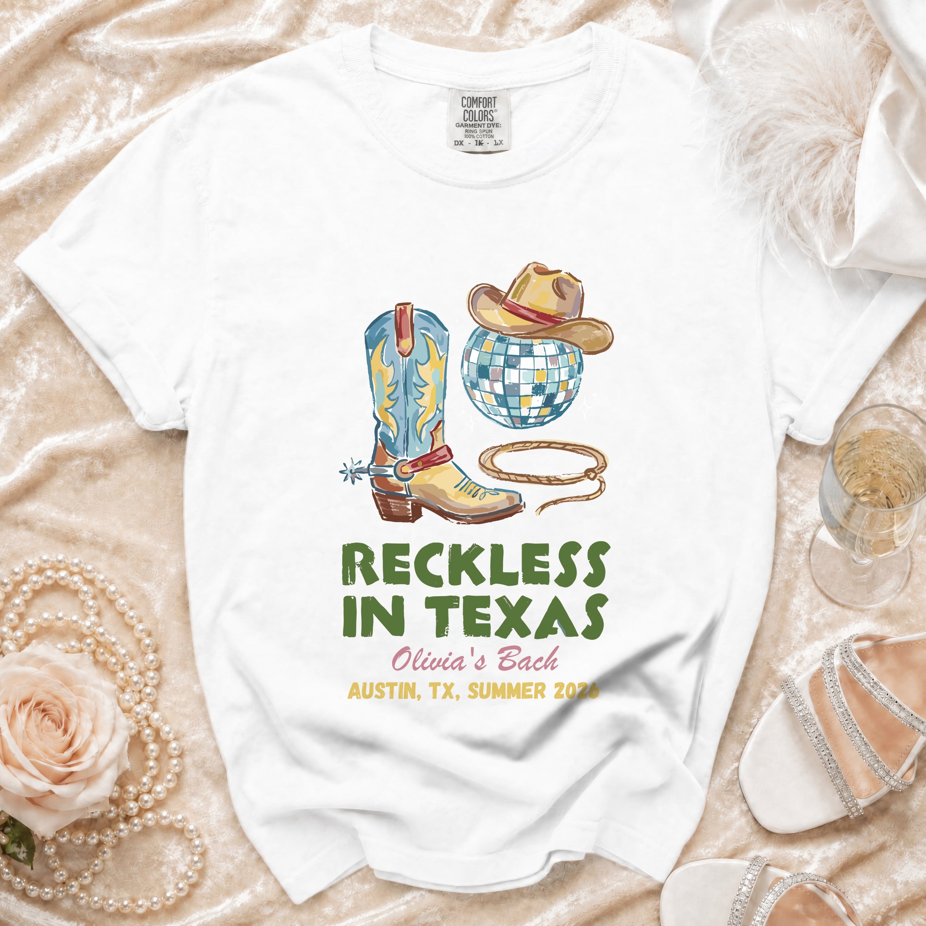 White t-shirt with cowboy boot, hat, disco ball, and text "Reckless in Texas".
