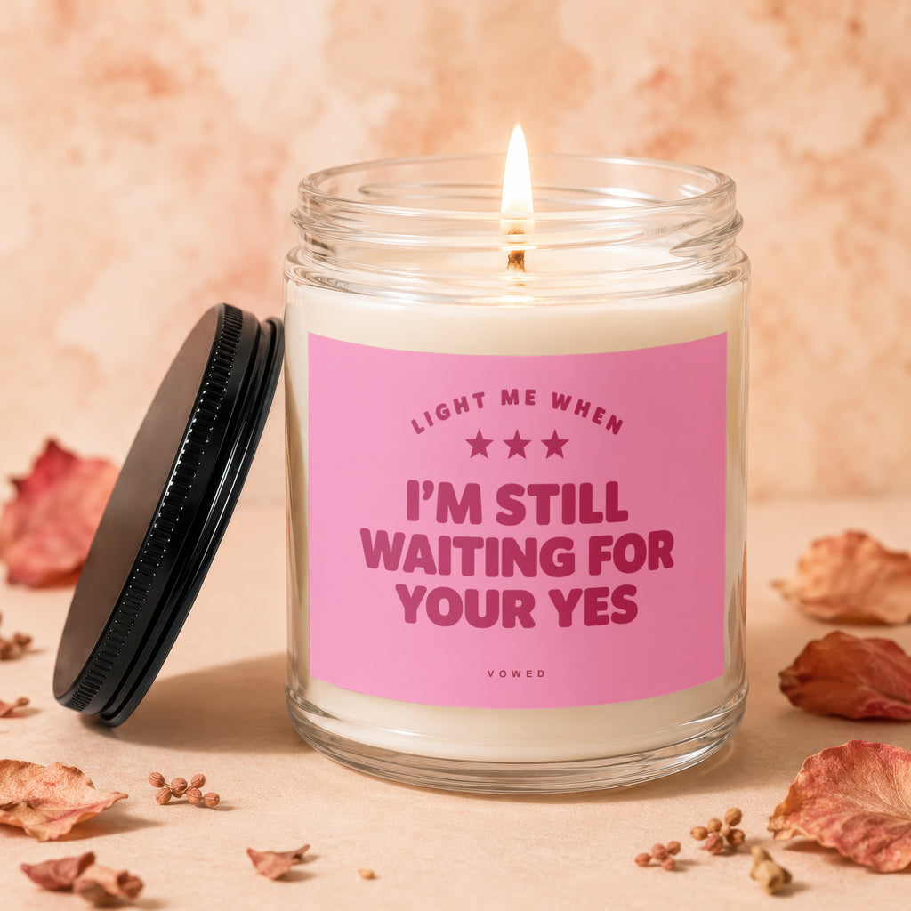 Candle with pink label reading "I'm still waiting for your yes".