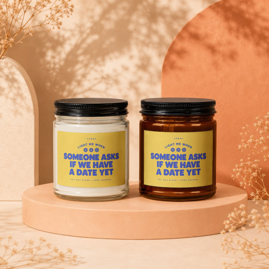 Two scented candles with yellow labels reading "light me when someone asks if we have a date yet."