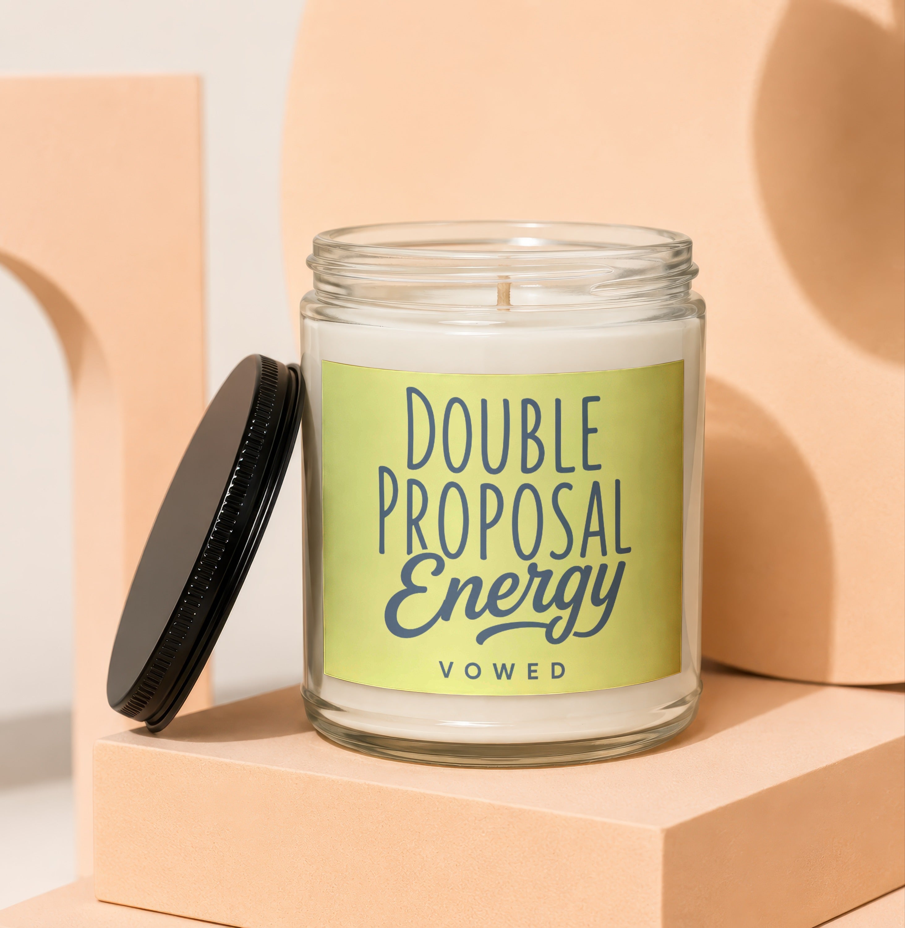 Glass candle with "Double Proposal Energy" and "VOWED" text on a light green label.