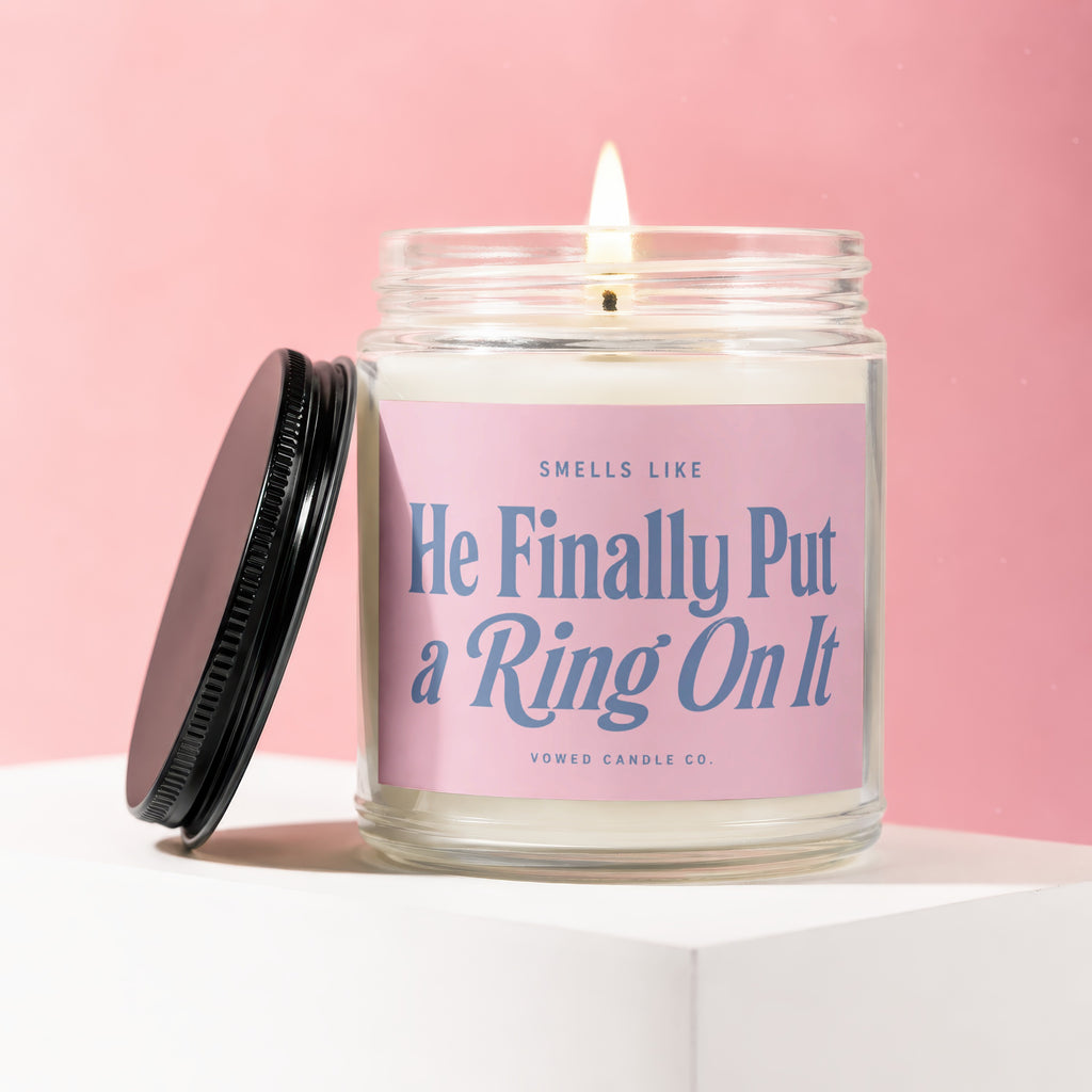 Candle labeled "He Finally Put a Ring On It Smells Like" on pink background.