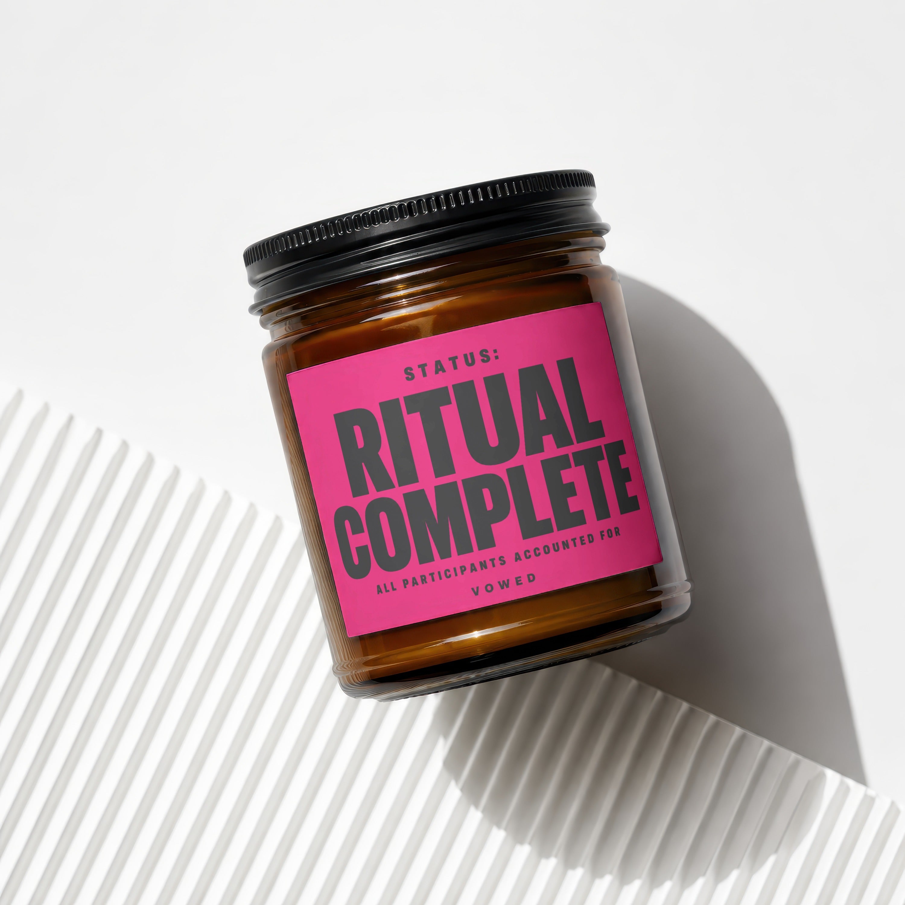 Amber glass jar candle with pink label that reads "STATUS: RITUAL COMPLETE"