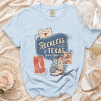 Light blue t-shirt with "Reckless in Texas" graphic and cowboy boot.