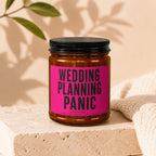 Amber jar candle with black lid and pink label that reads "Wedding Planning Panic Loading..."