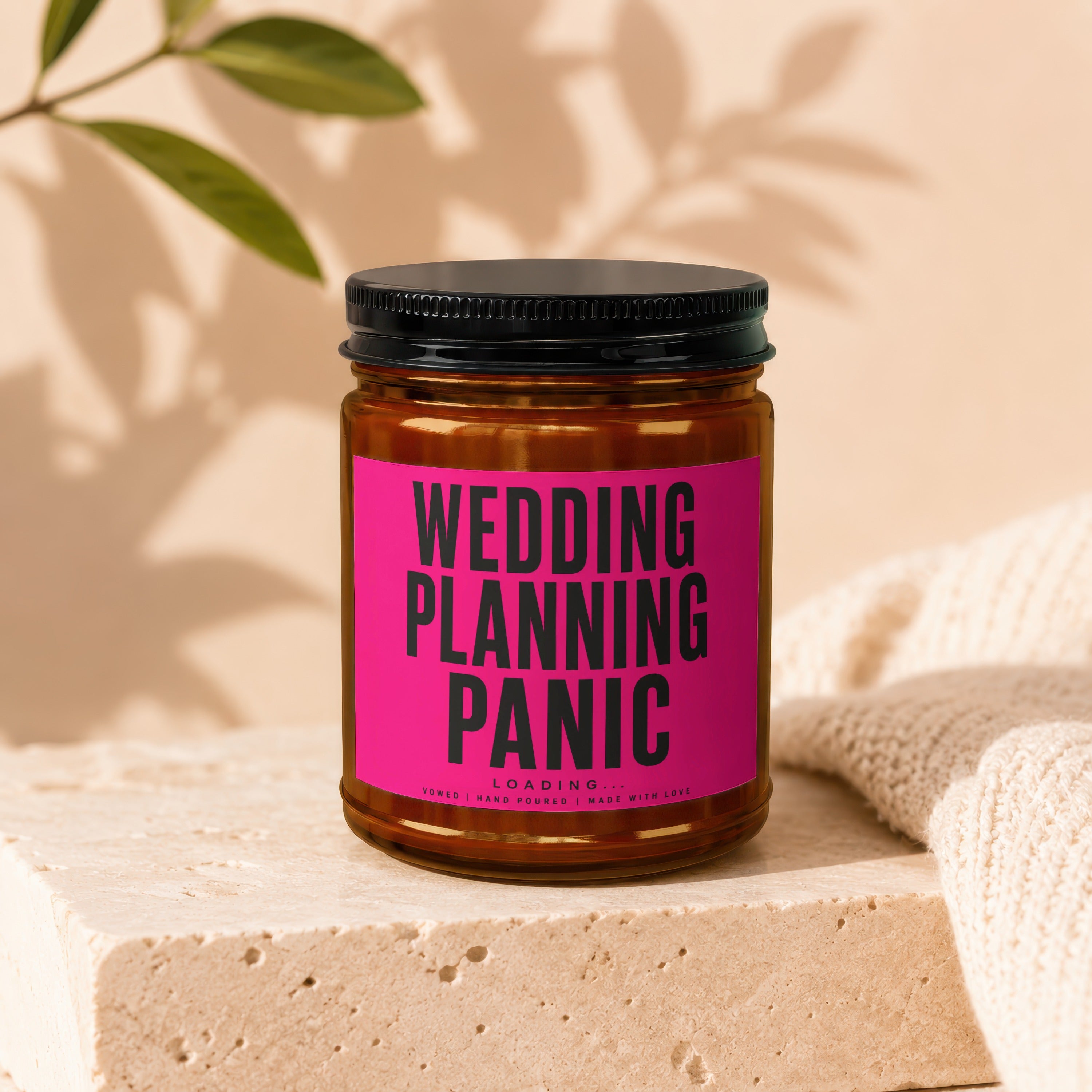 Amber jar candle with black lid and pink label that reads "Wedding Planning Panic Loading..."