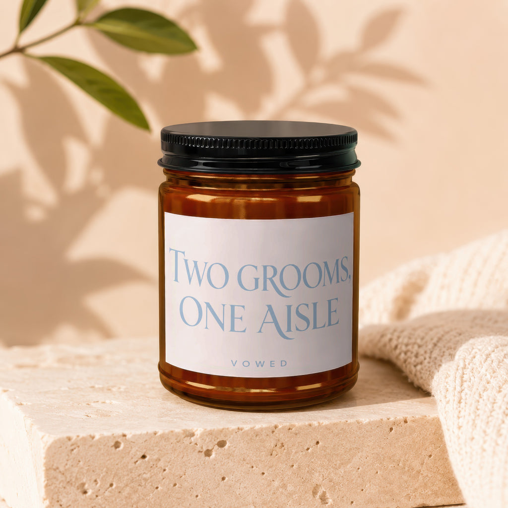 Candle with "TWO GROOMS ONE AISLE" text on label, next to knit fabric.