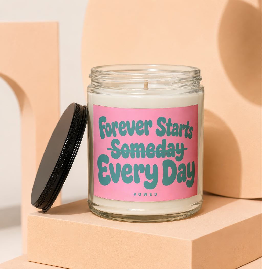 Glass candle with pink label that reads "Forever Starts Someday Every Day Vowed".