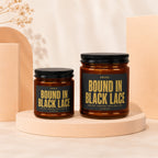 Two amber glass candles with black lids and labels reading "Bound in Black Lace."