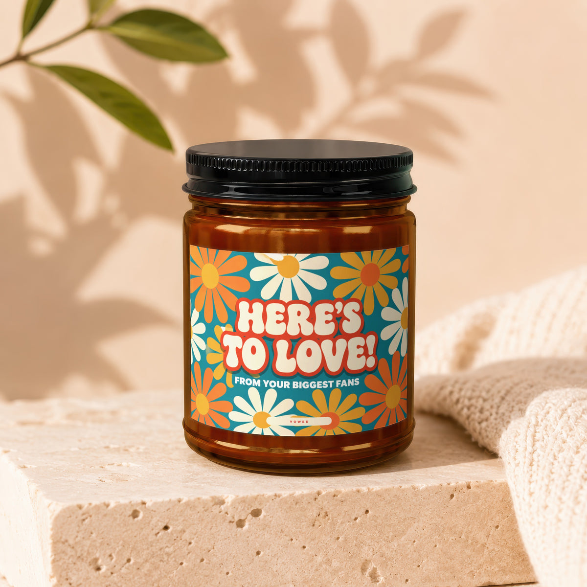 Candle with "Here's to Love! From Your Biggest Fans" text and daisy design.