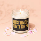 Lit candle in a glass jar with black label reading "DISTANCE AIN'T SH*T VOTED"