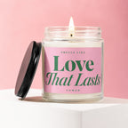 Candle in a glass jar with pink label reading "Love That Lasts" and "vowed".