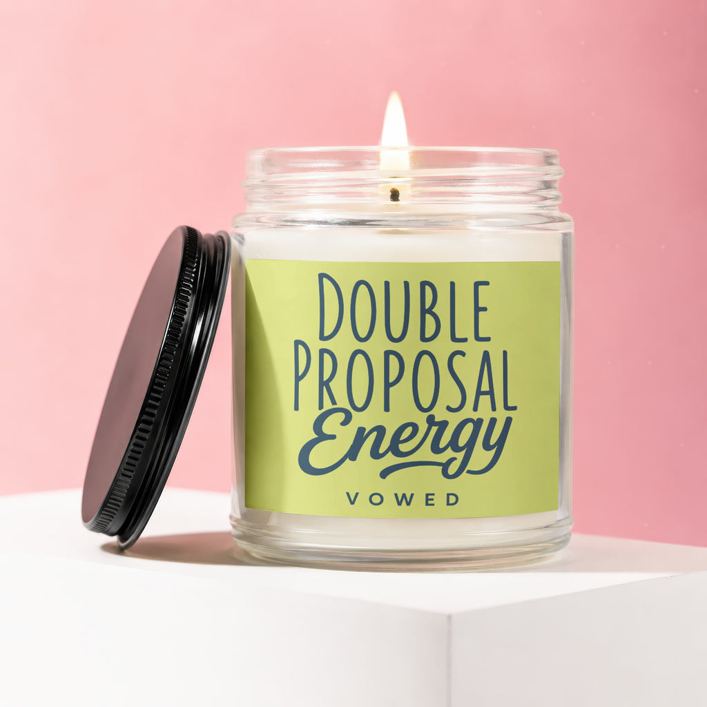 Lit glass jar candle with "DOUBLE PROPOSAL ENERGY" and "vowed" on a lime green label.
