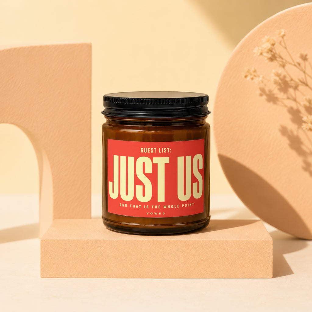 Amber candle with "JUST US" and "VOWED" text on red label, on pedestal.