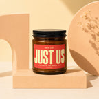 Amber candle with "JUST US" and "VOWED" text on red label, on pedestal.