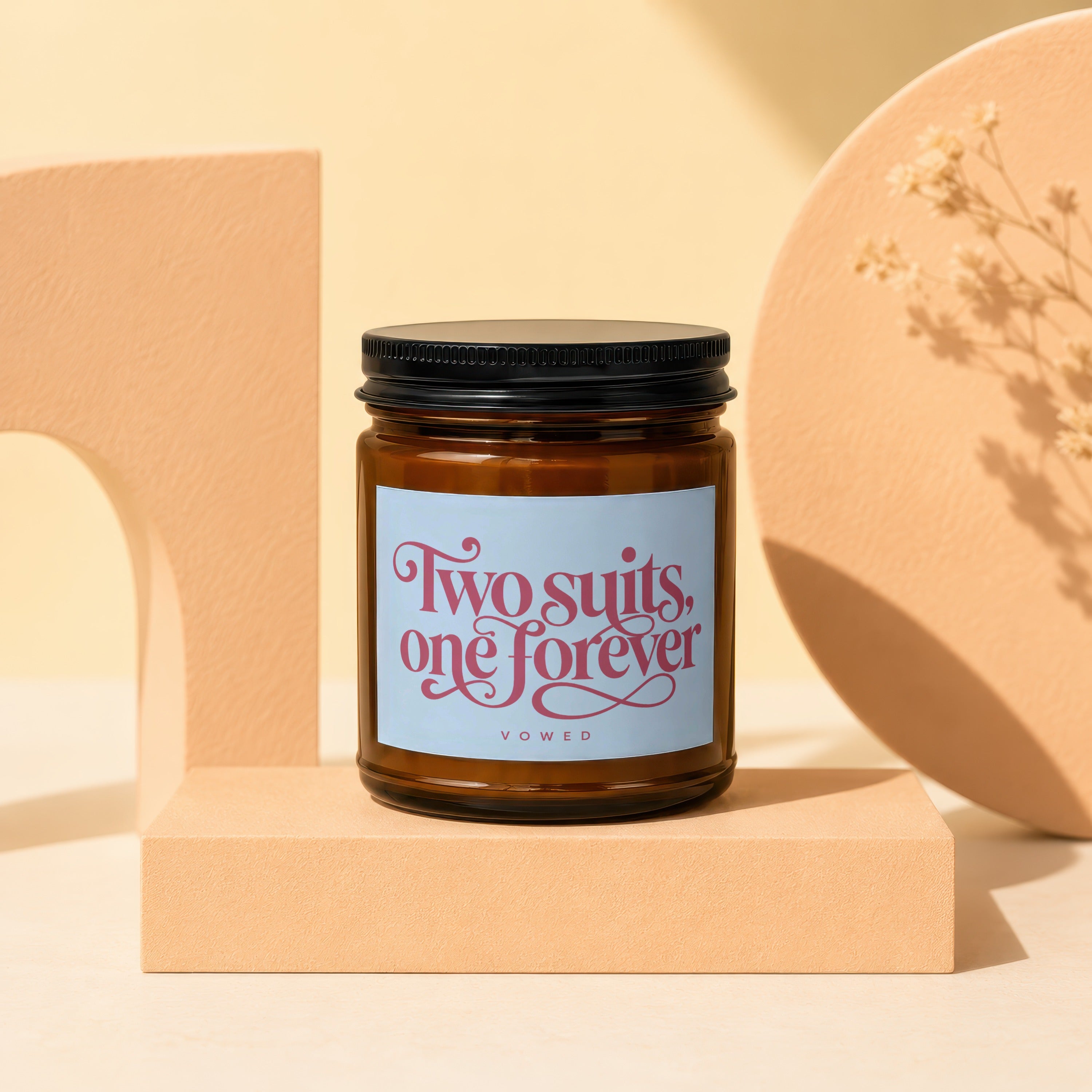 Amber jar candle with black lid, label reads "Two suits, one forever VOWED".