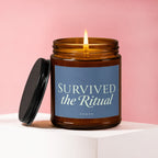 Amber jar candle with lit flame and lid, reading "SURVIVED the Ritual"