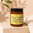 Amber jar candle with yellow label reading "You're Legally Required to Say Yes"
